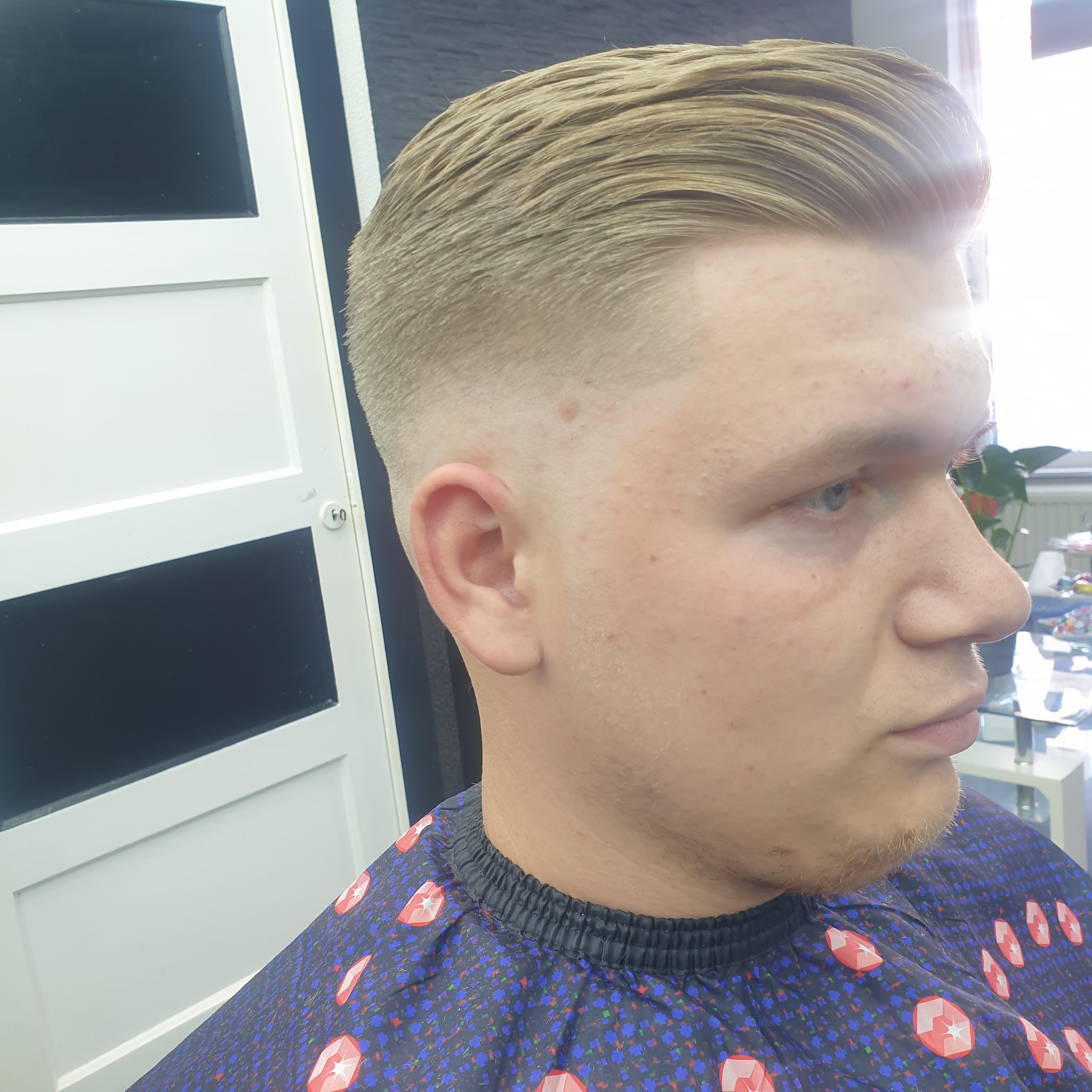 Blonde slick back met een hoge skin fade, van opzij gefotografeerd