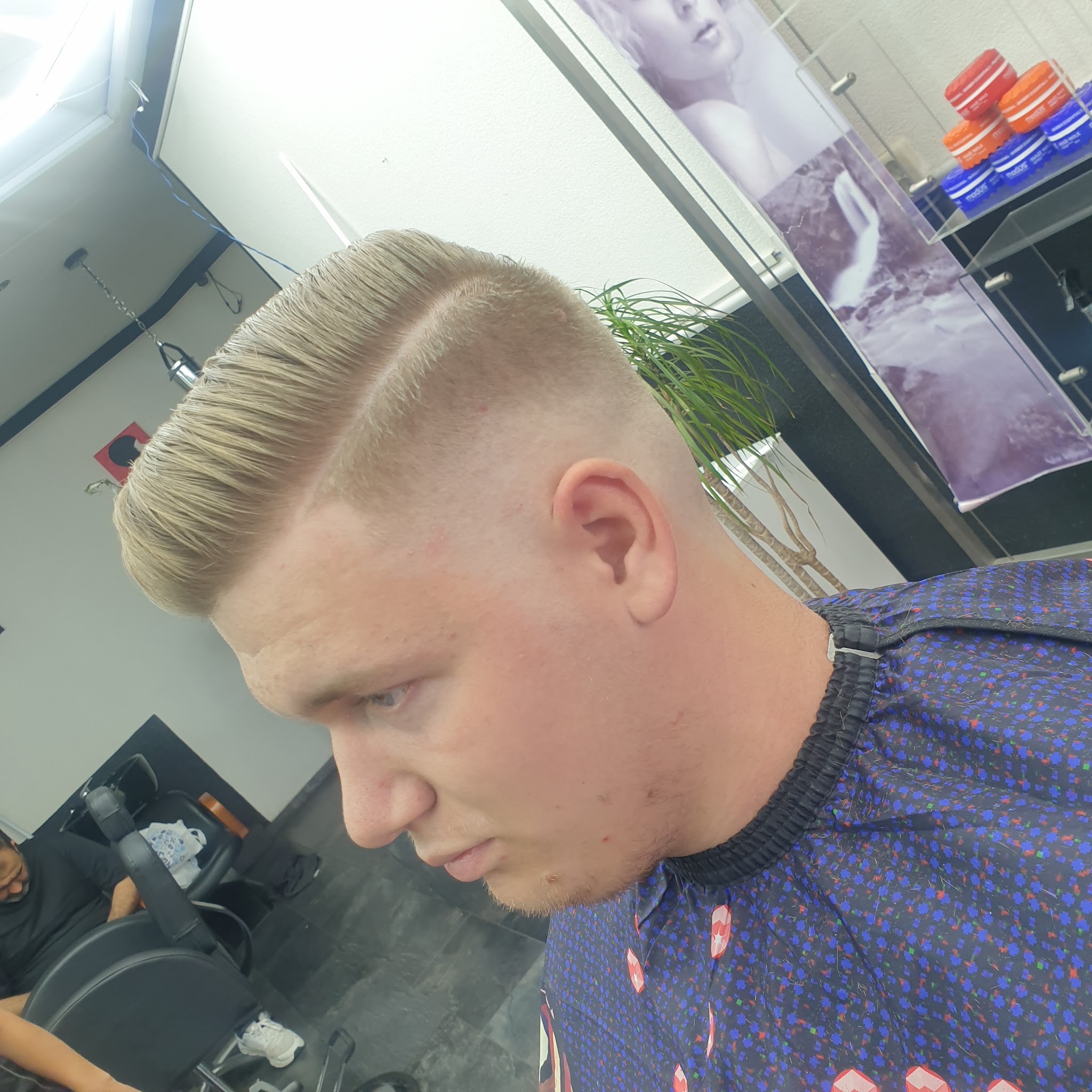 Blonde pompadour met een strakke fade, met het productschap van de zaak op de achtergrond